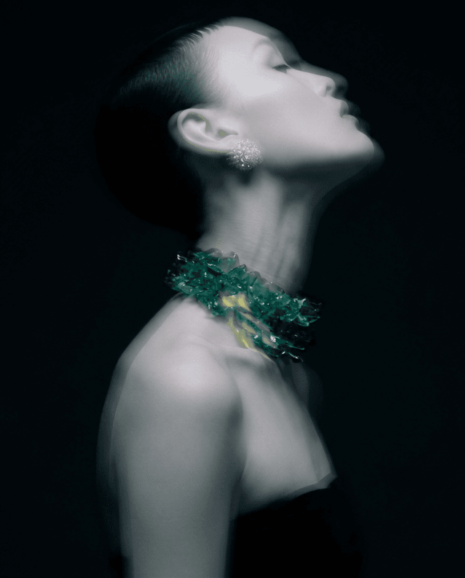 Profile view of a woman with blurred background, dark tones, and green and yellow jewellery.