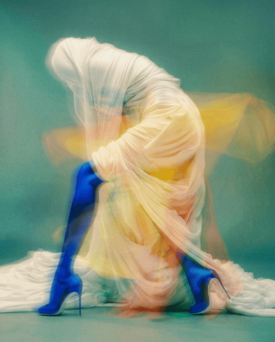 A distorted figure covered in flowing iridescent fabric with vibrant blue, yellow, and orange colours.