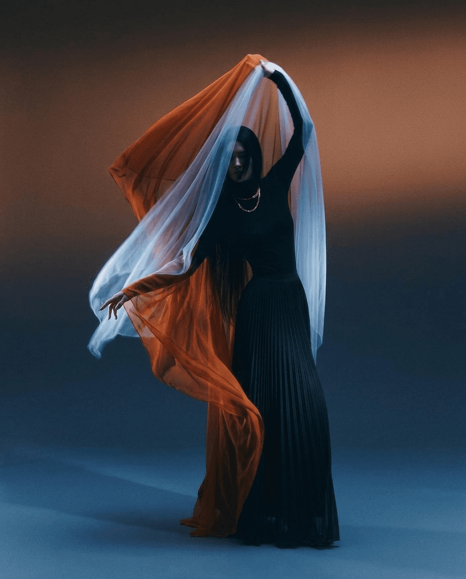 A woman poses elegantly in a flowing garment with contrasting orange and blue hues.