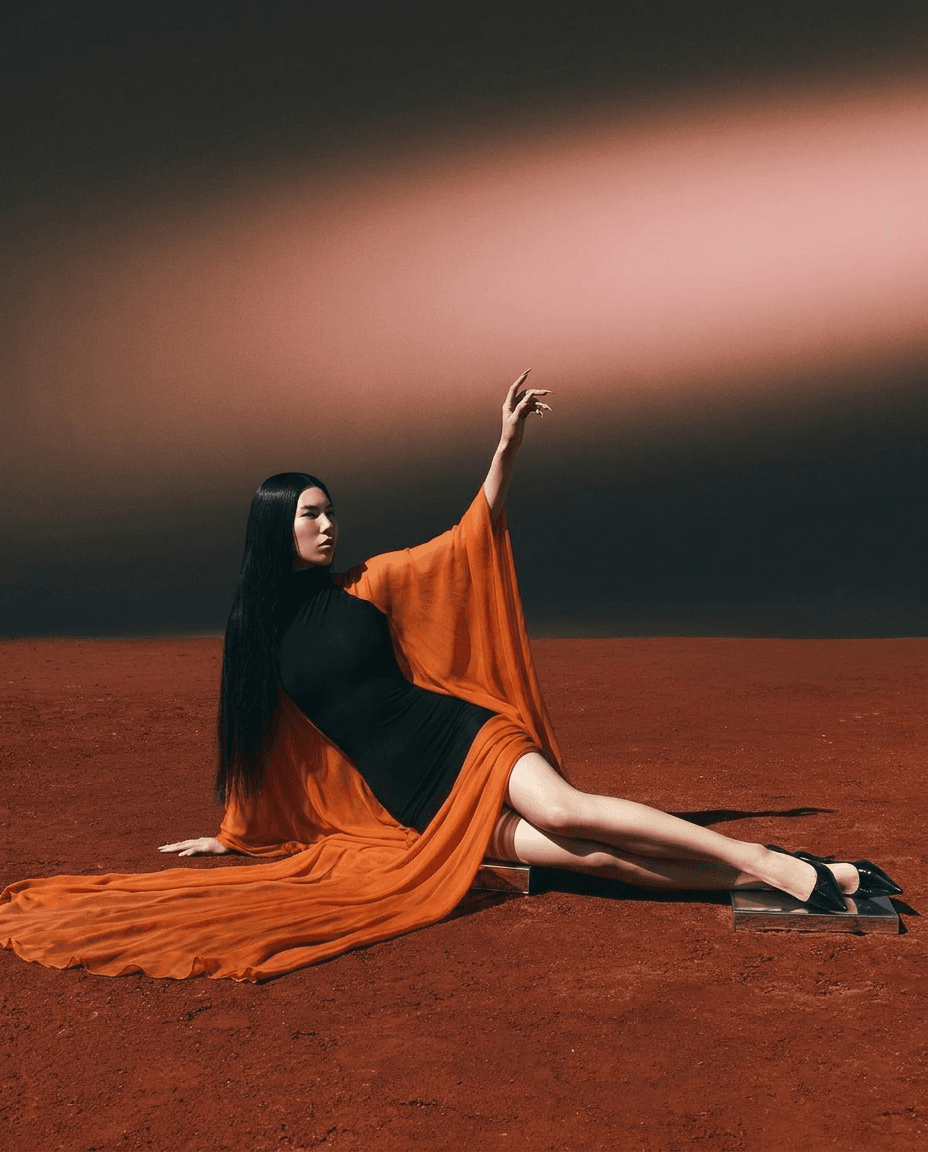 Woman in an orange dress posed against a reddish-brown background.
