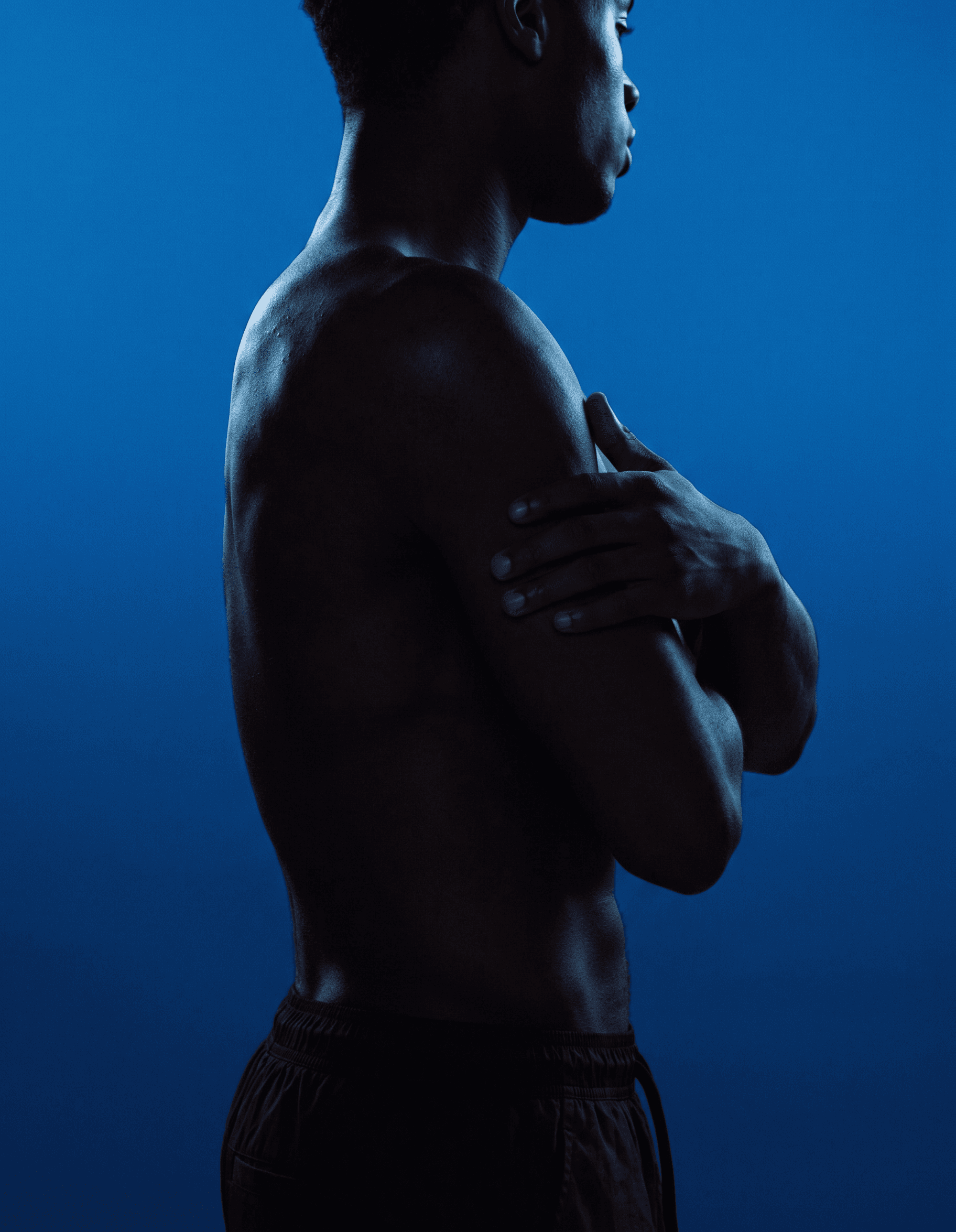 Profile view of a man with crossed arms and a strong physique in deep blue tones.