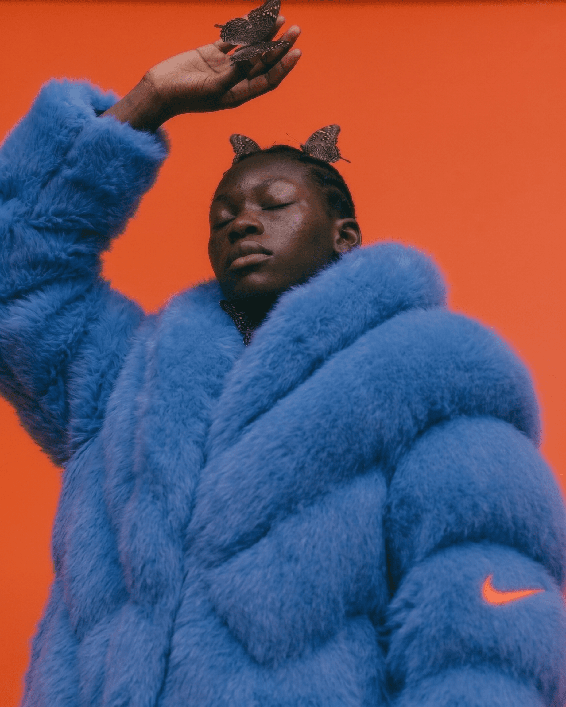 Portrait of a woman with closed eyes in a blue coat against an orange background.
