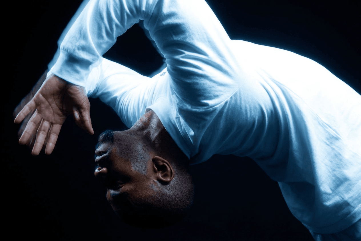 Full-figure portrait of a man dancing in blue lighting against a dark background.