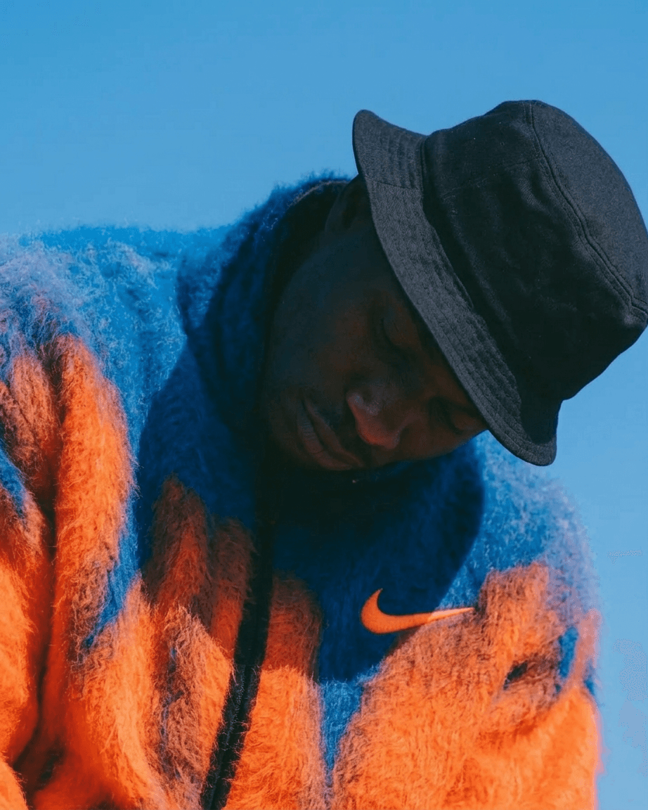 Portrait of a man wearing an orange and blue sweater and a black bucket hat.