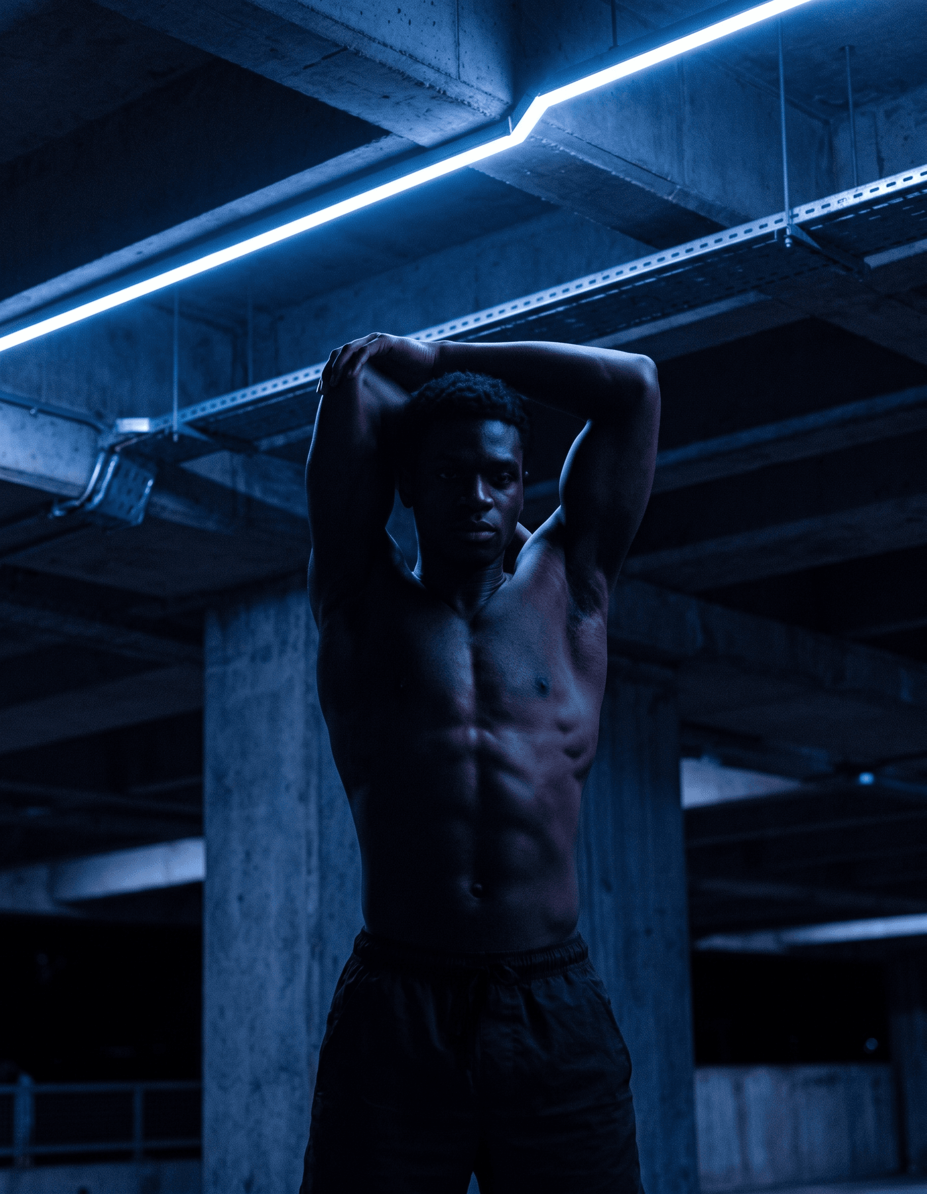 Shirtless man posing in a dimly lit area with neon blue lights.