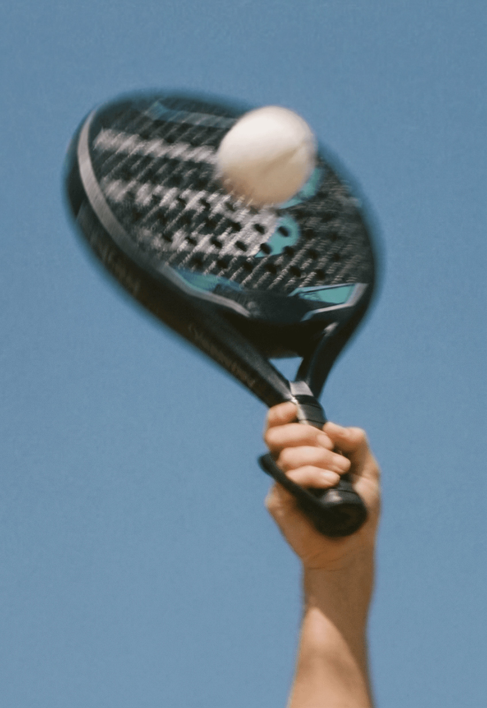 A hand holding a tennis racket in motion, hitting a ball with a blue sky background.