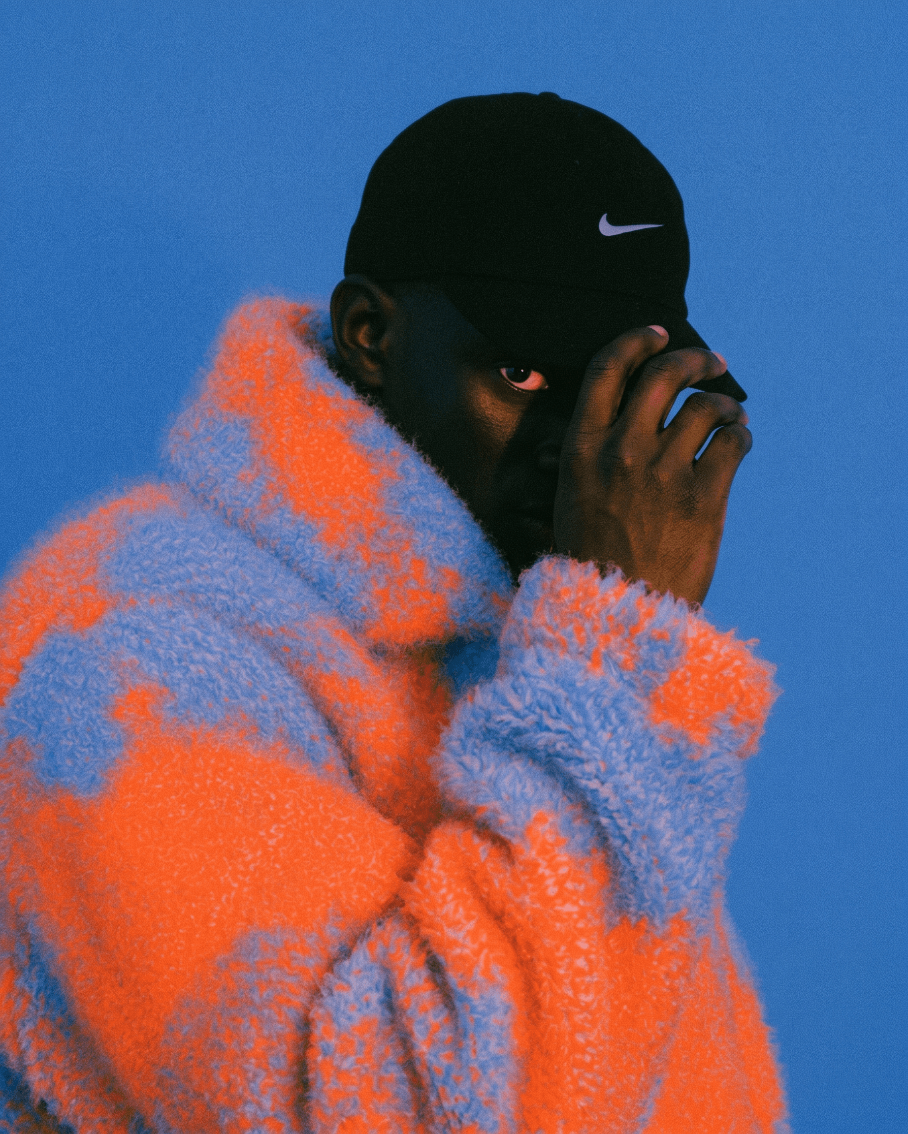Man wearing a vibrant orange and blue fuzzy sweater with a blue background.