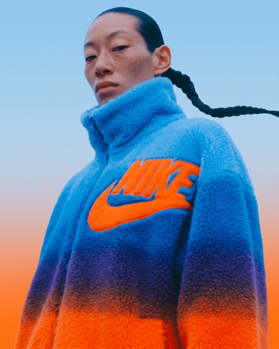 A woman in a fleece jacket with a logo, set against a blue and orange gradient background.