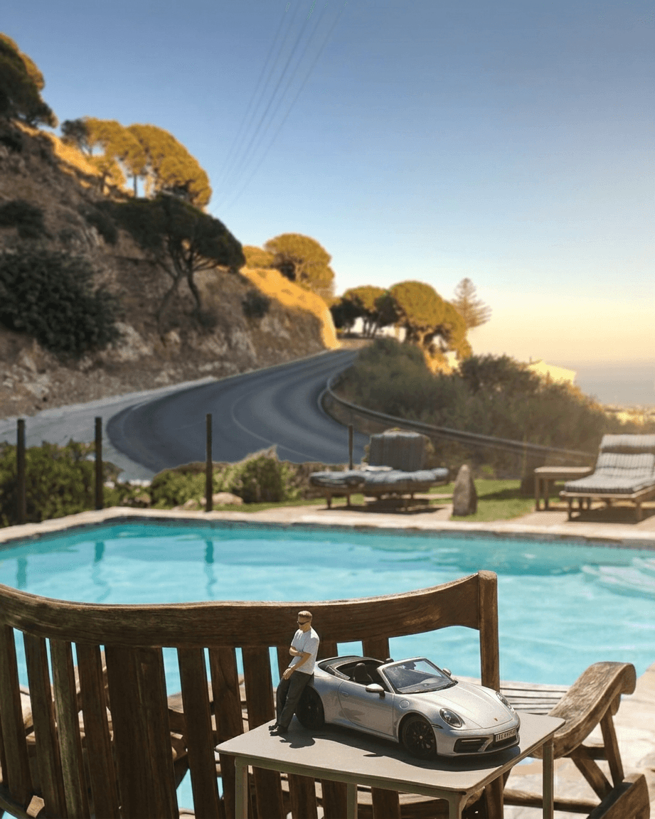 Model car next to a pool with a coastal road in the background.