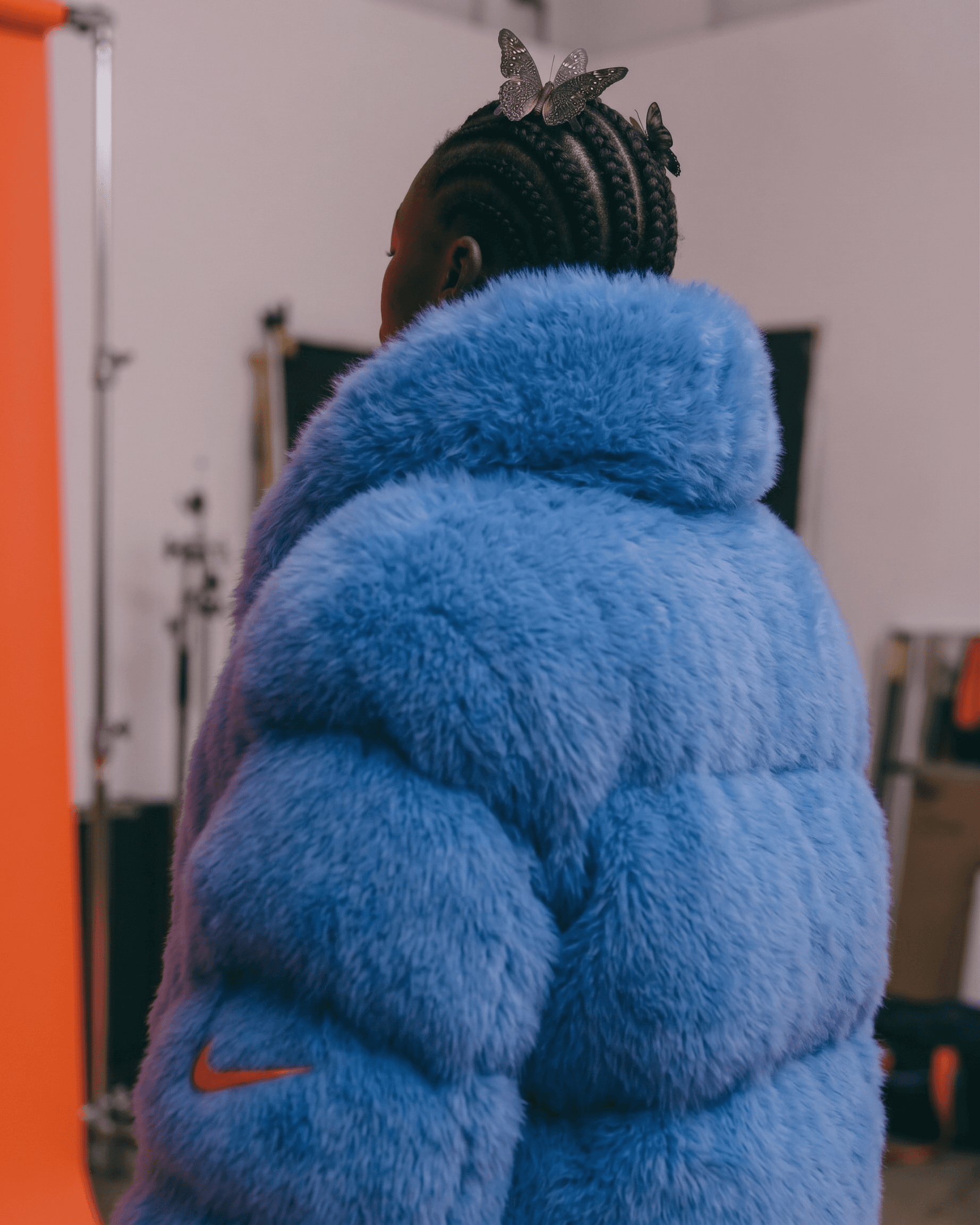 Woman in a puffy blue coat standing in front of an orange backdrop.