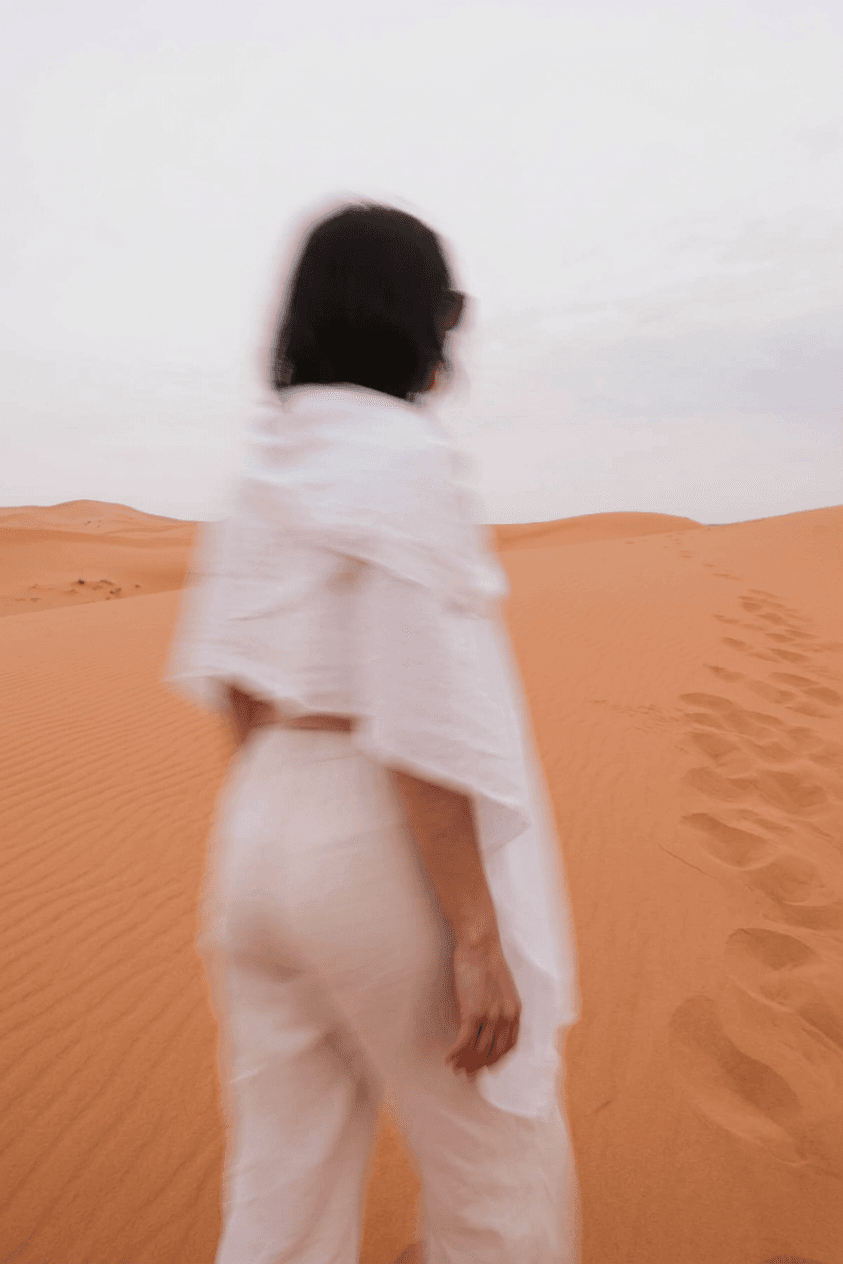 A woman dressed in white walks across a tranquil desert landscape.