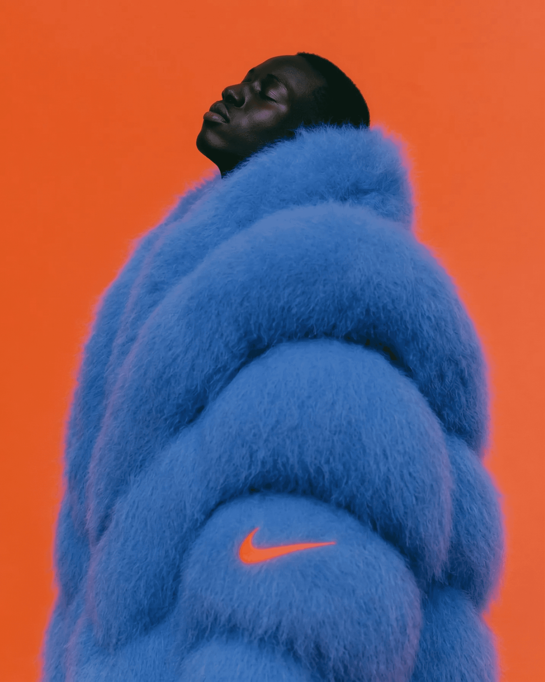 Portrait of a man wearing a blue fluffy jacket with an orange background.