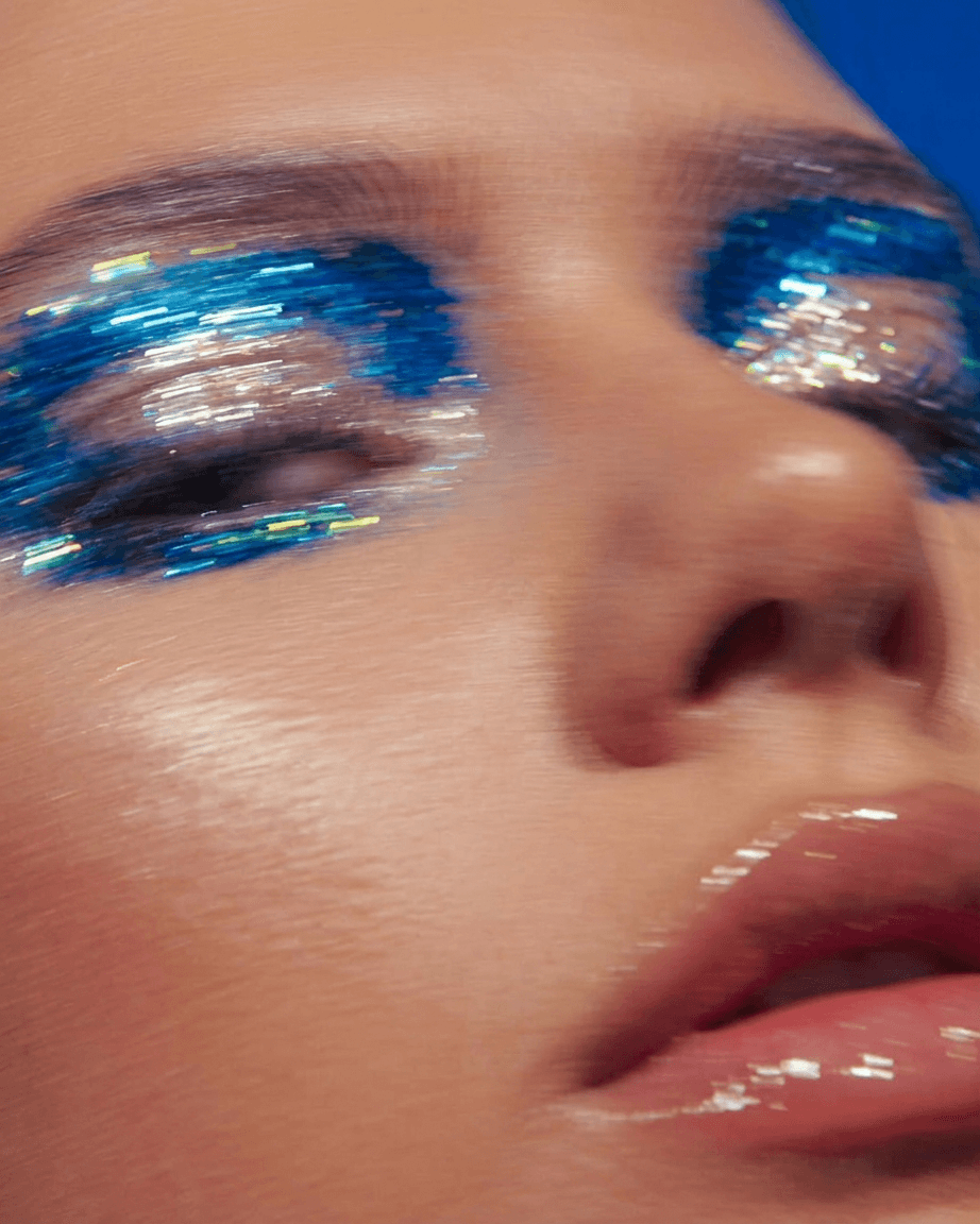 Close-up of a woman's face with bold blue and silver sparkly eye makeup.