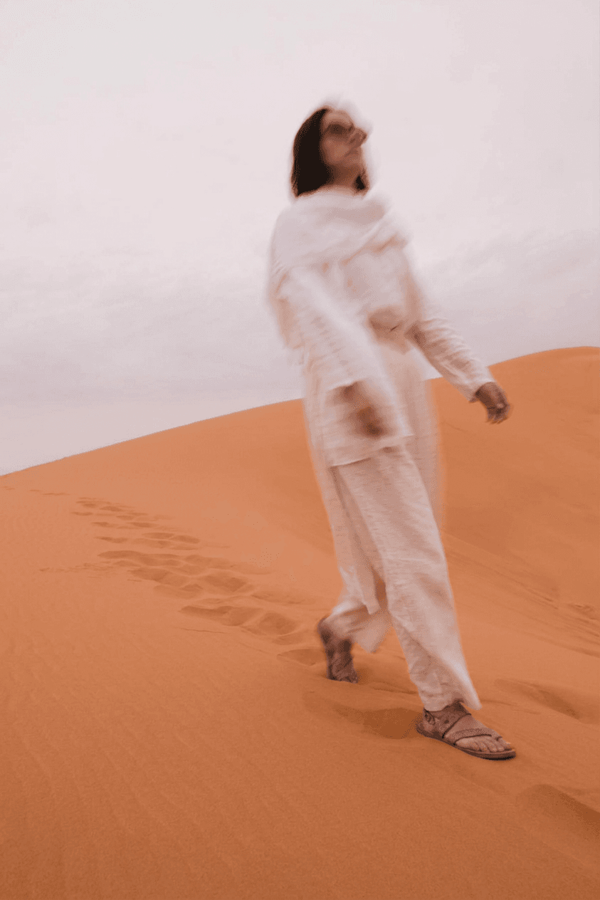 A woman walking in a sandy desert landscape with soft tones.