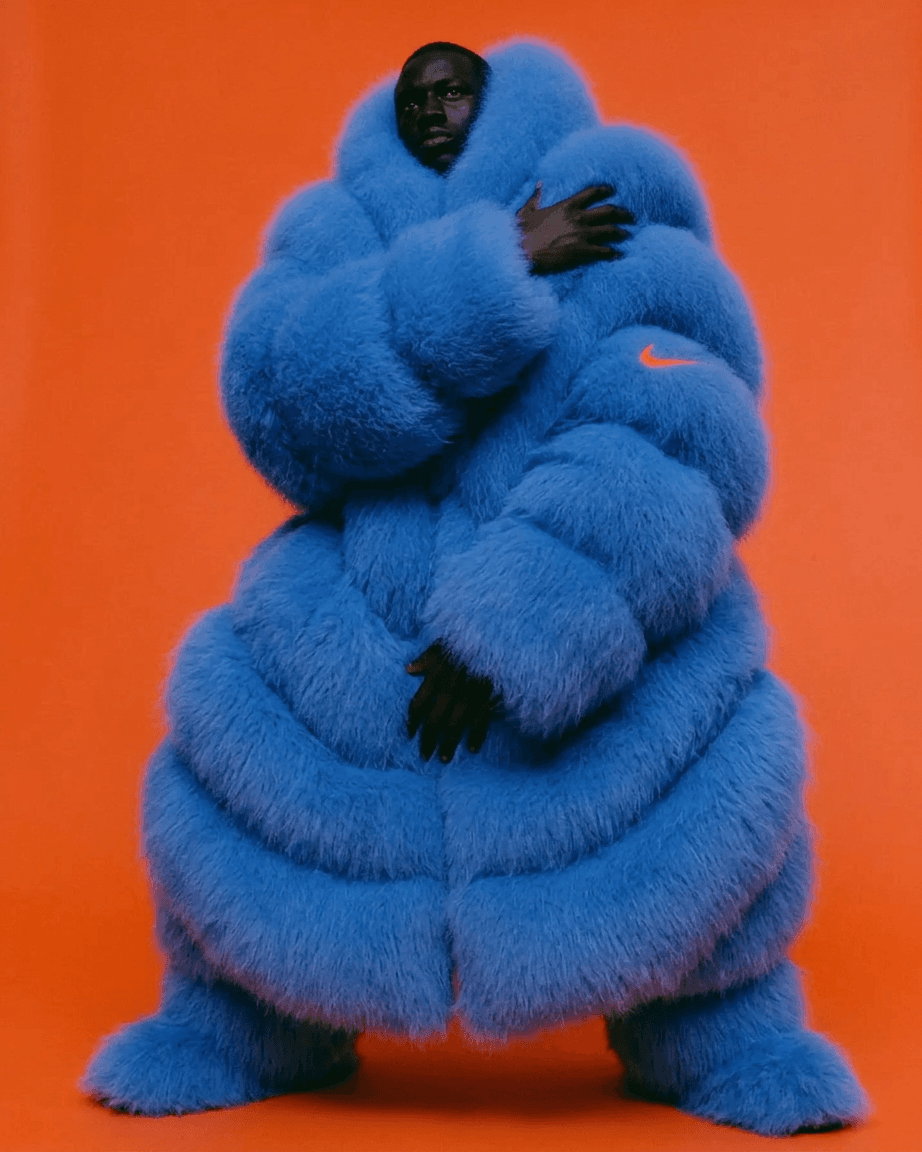 Portrait of a man wearing a blue fur coat with an orange background.