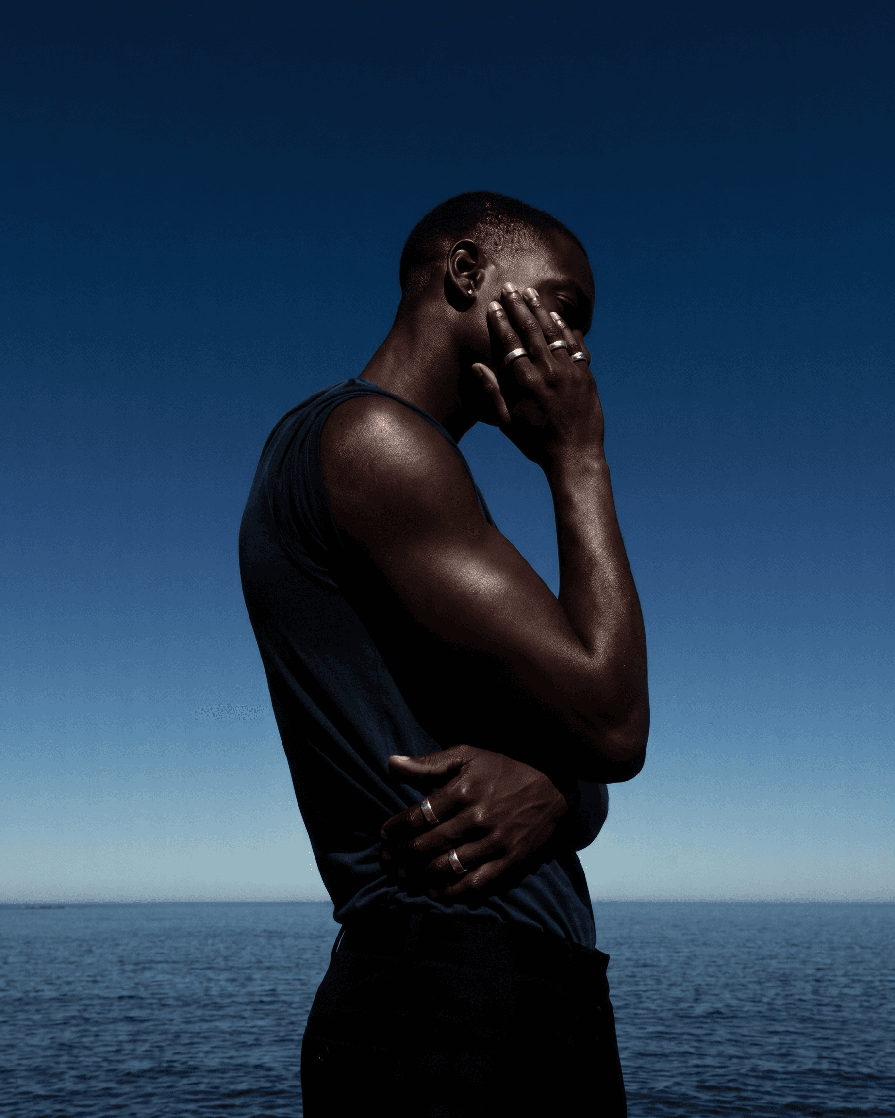 Profile of a man standing by the ocean with a clear blue sky.