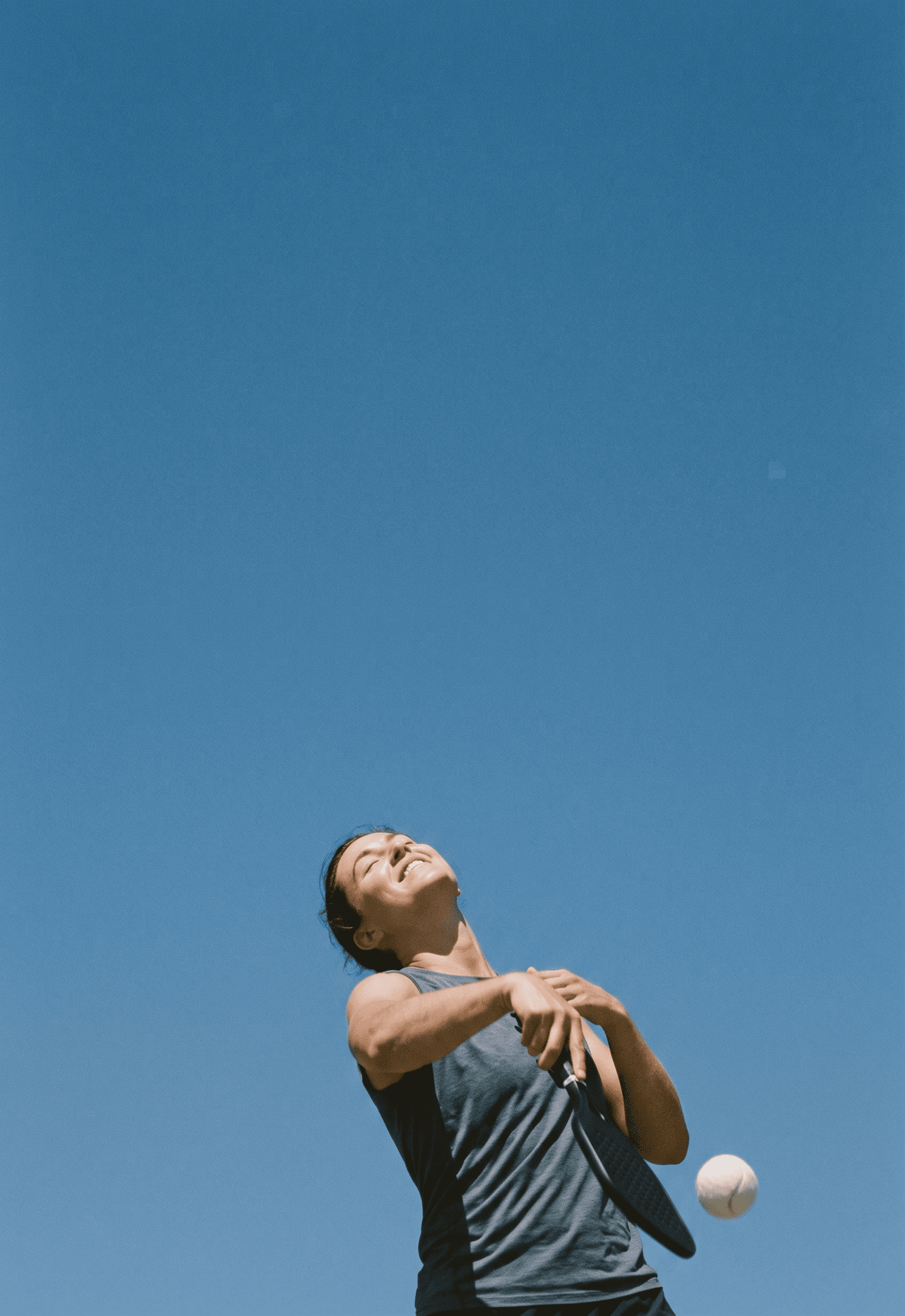 A young woman swings a tennis racket under a clear blue sky.