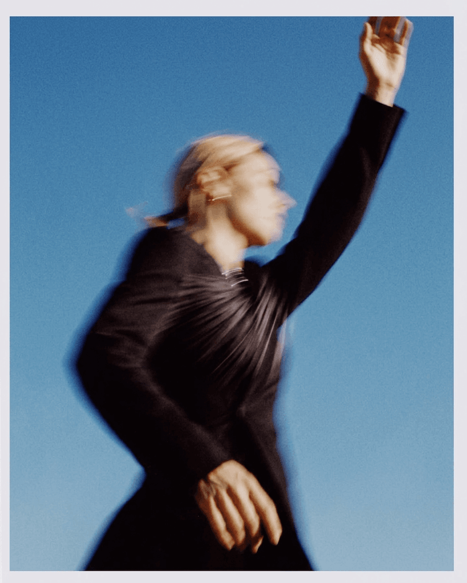 A blurred figure of a woman moving against a clear blue sky.