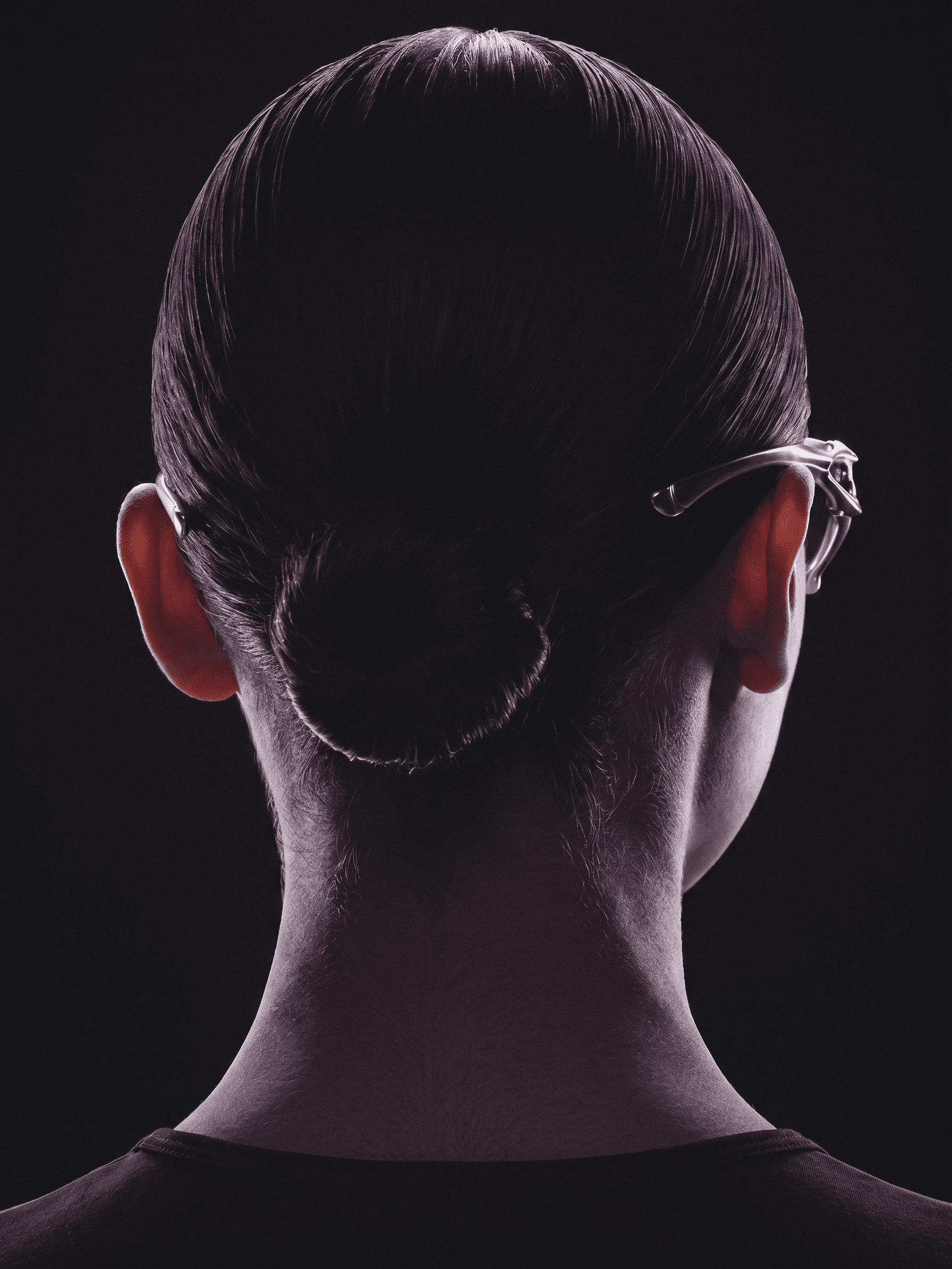 Back view of a woman with a sleek bun hairstyle and glasses.
