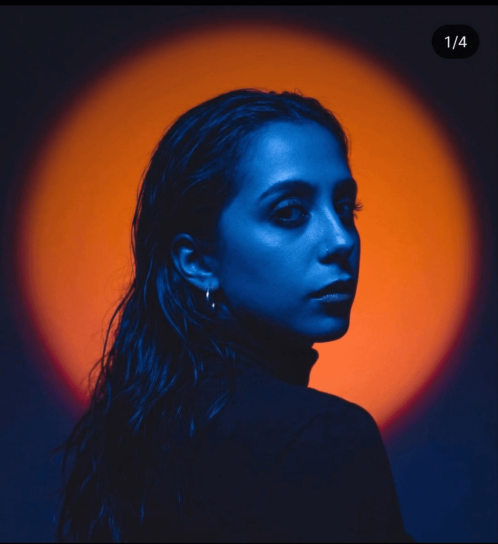 Portrait of a woman facing away, illuminated by blue light with an orange background.