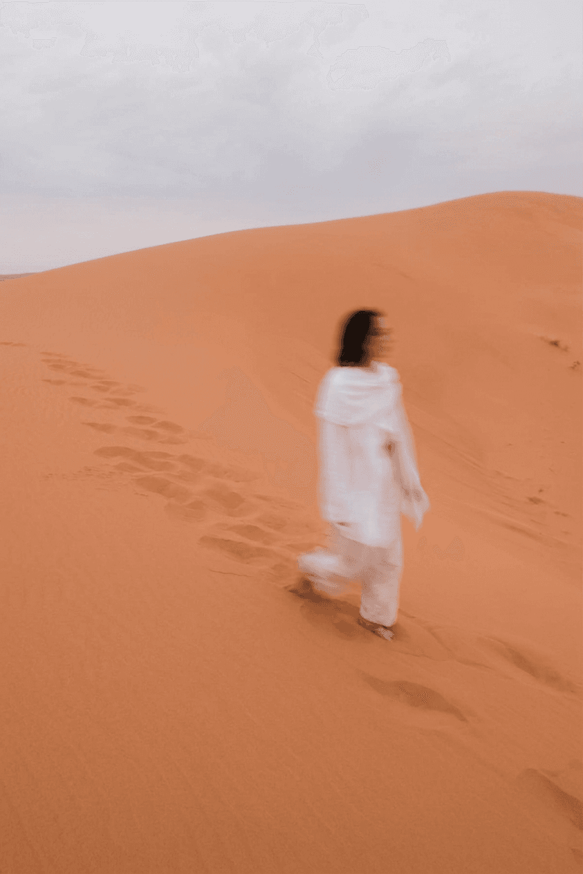 A blurred figure of a woman walking on an orange sand dune.