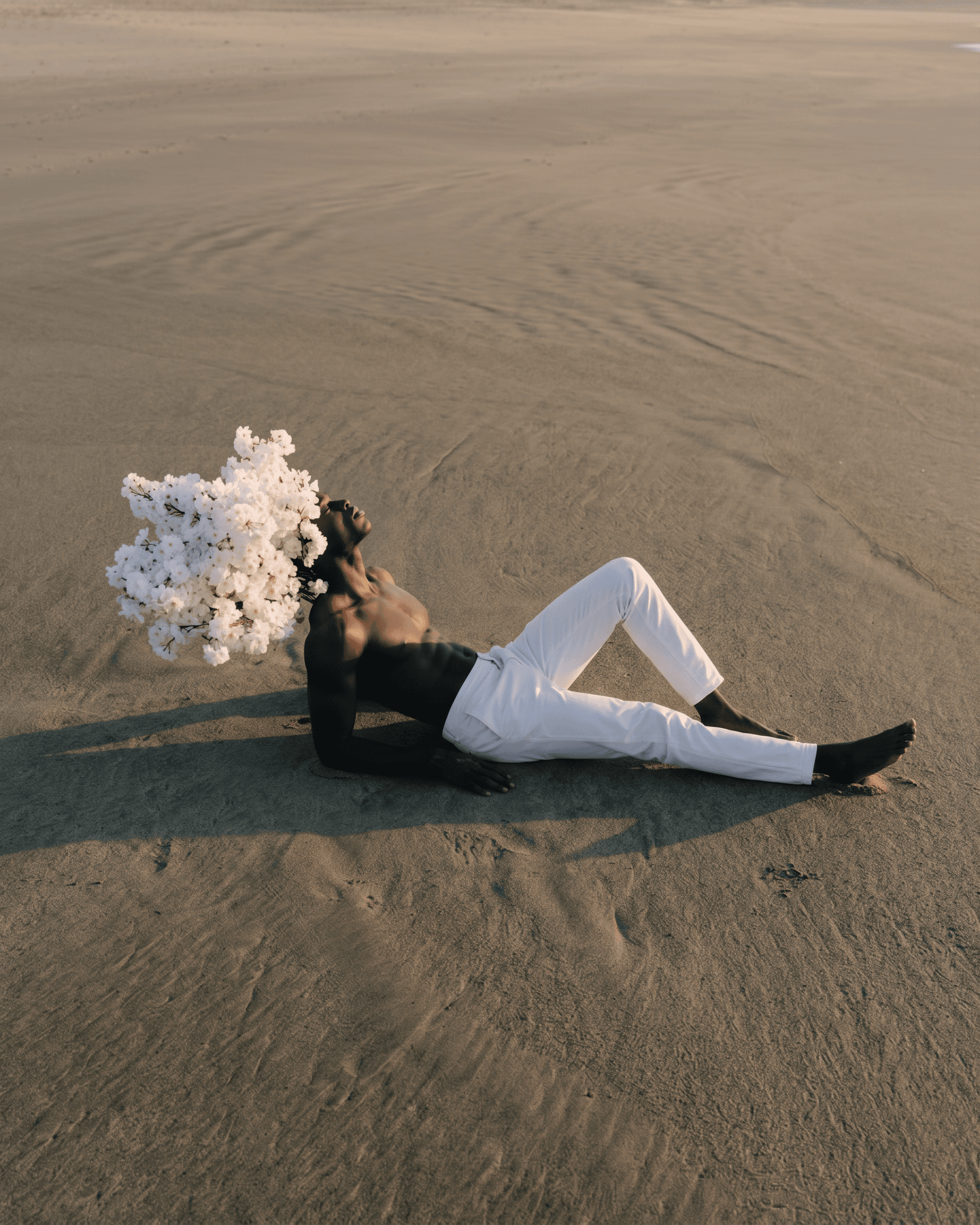 A man lying on a sandy beach wearing a floral headpiece.