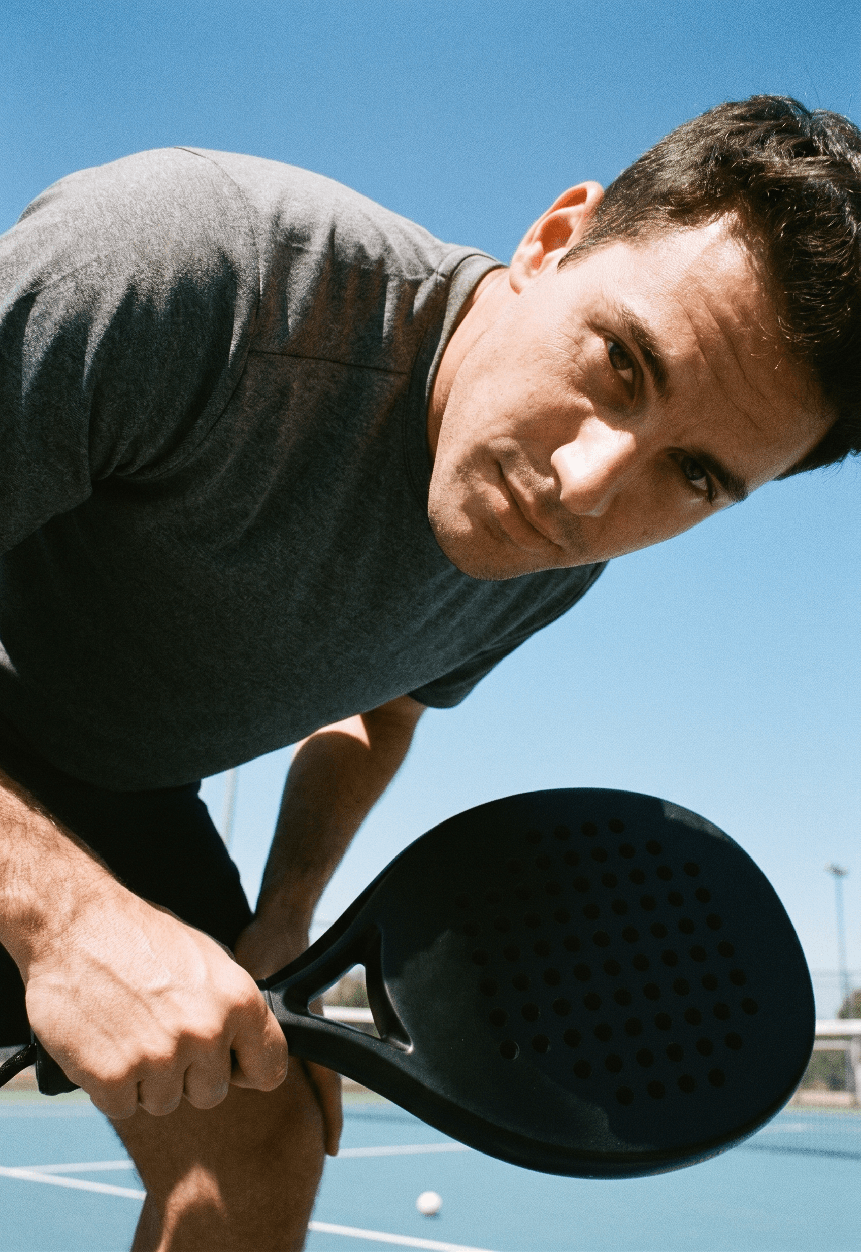 Man with a focused expression holding a black paddle, leaning forward under a blue sky.