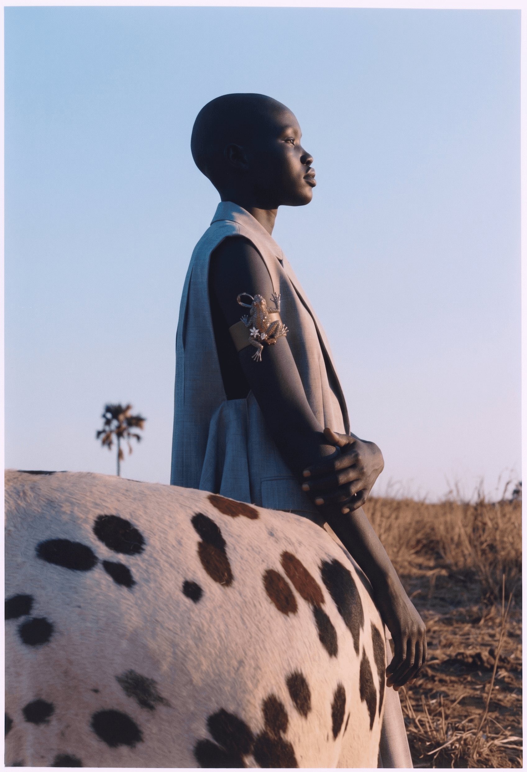Profile view of a woman standing next to a speckled cow with a pastel sunset sky.