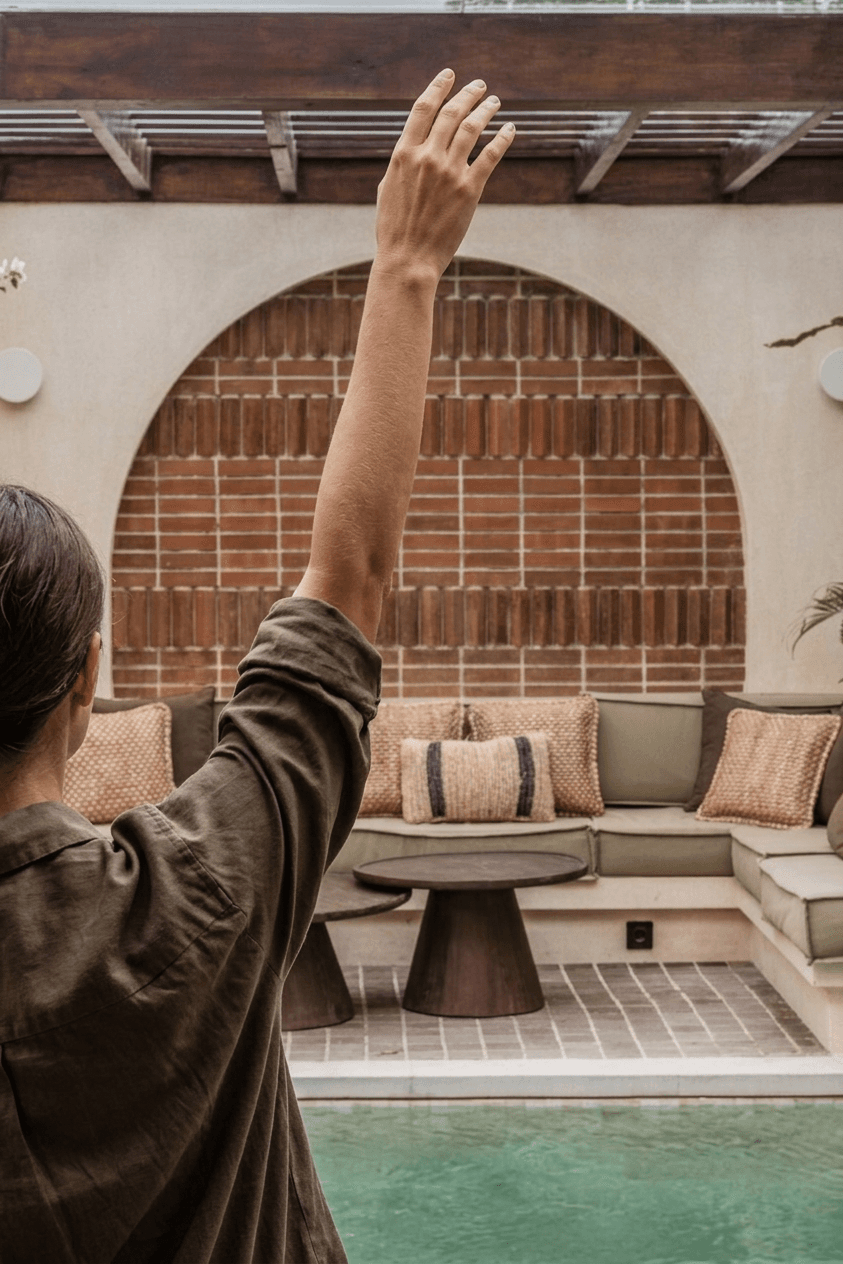 A woman with her arm raised in a serene outdoor lounge area by the pool.