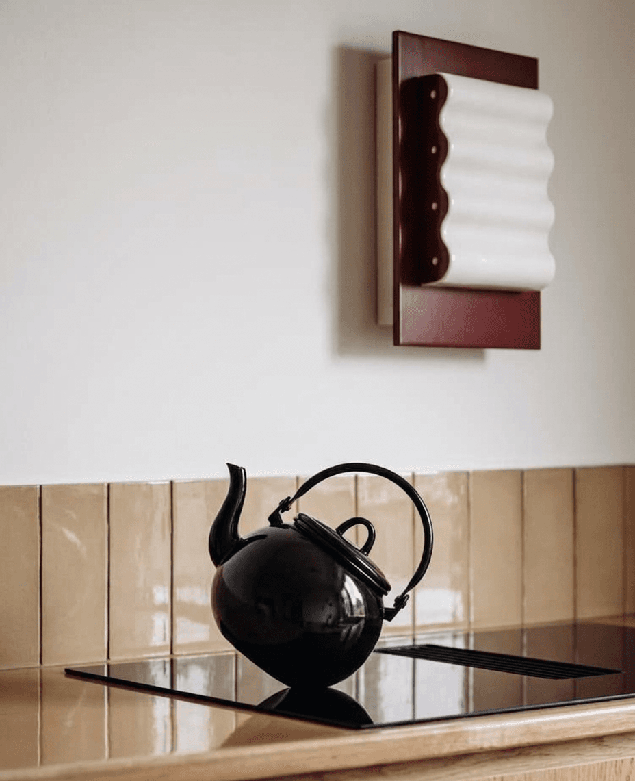 A black teapot and a decorative wall piece in a minimalist kitchen setting.