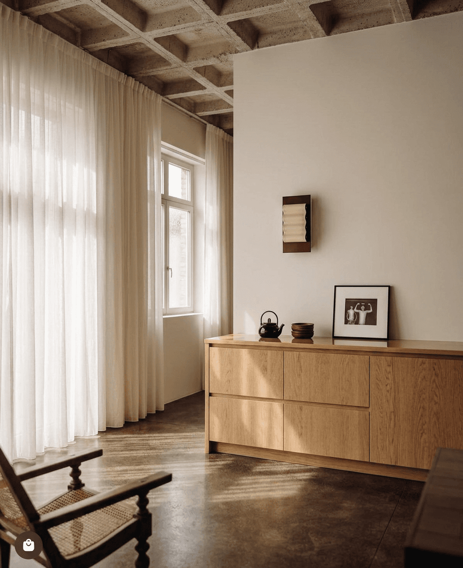 Cozy interior with a wooden cabinet, framed artwork, and a kettle in soft natural light.