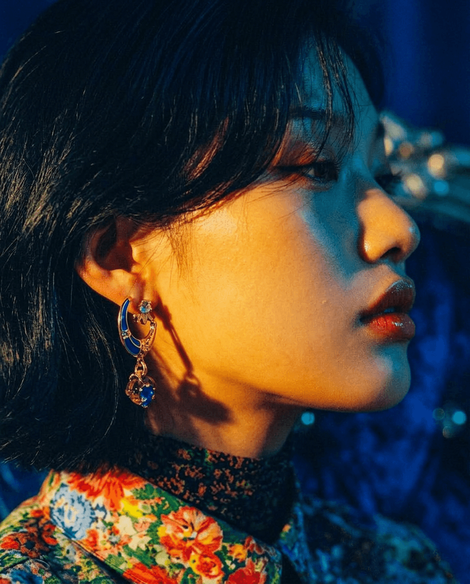 Profile of a young woman with earrings, vibrant blue background, floral-patterned outfit.