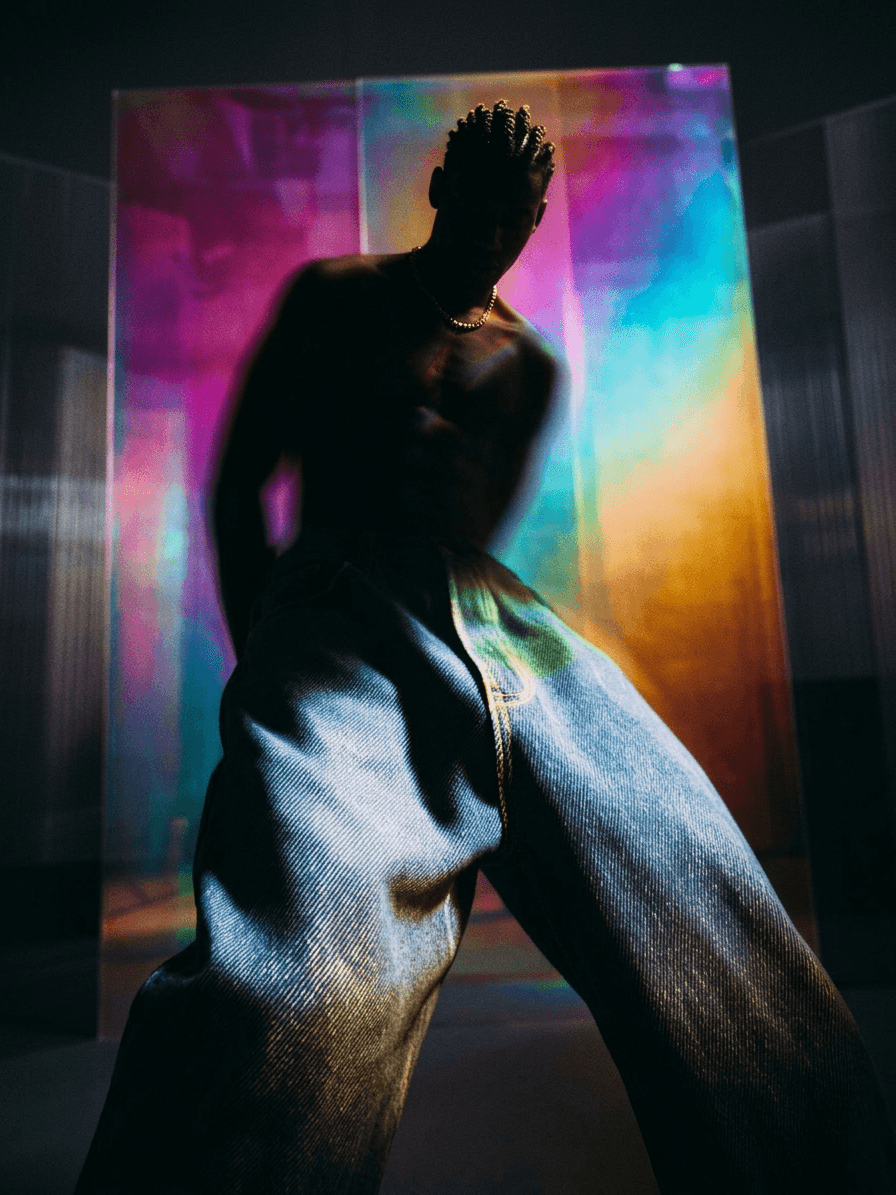 Silhouetted figure wearing oversized denim with an iridescent background.