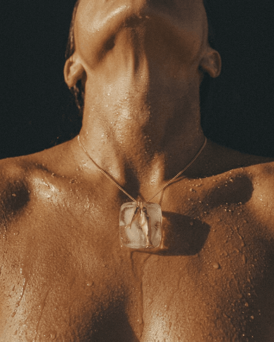 Close-up of a wet torso with an ice cube pendant on a dark background.