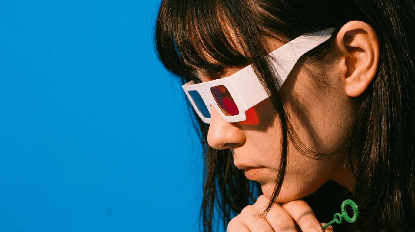 Close-up of a young woman with colourful 3D glasses on a blue background.