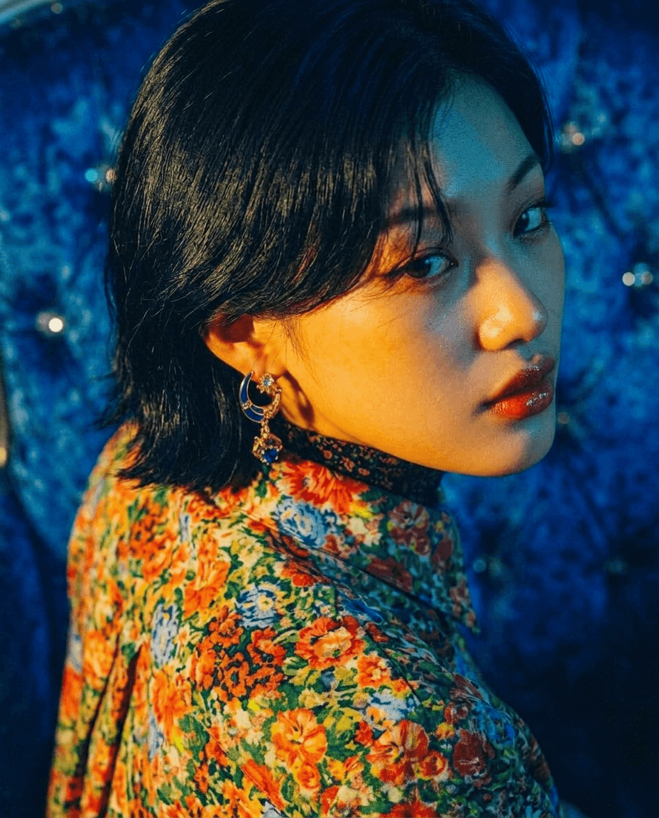 Young woman with dark hair in a floral blouse, displaying a contemplative expression.