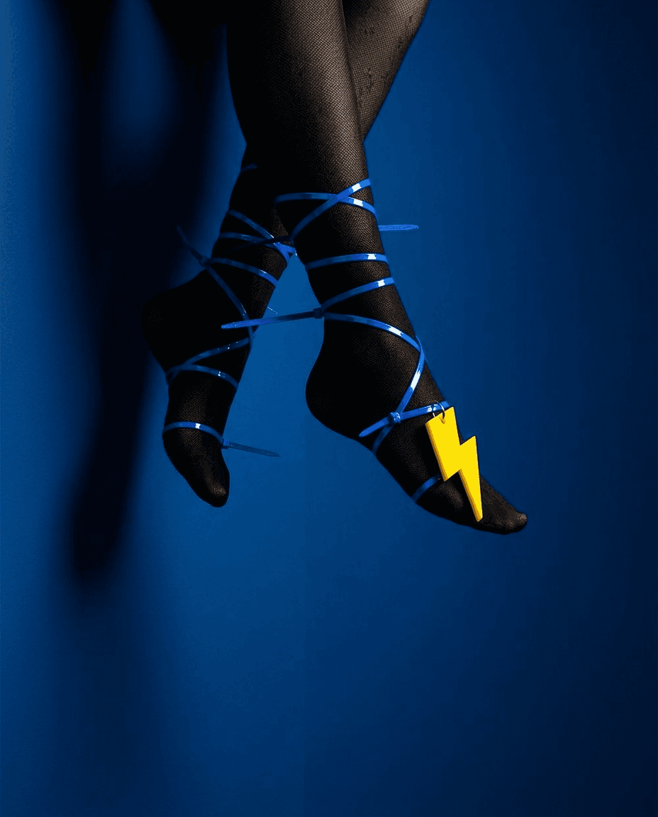 Close-up of feet in black stockings with blue ribbons and a yellow lightning bolt accessory.