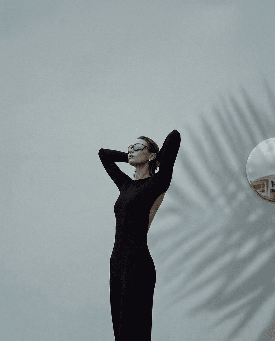 A model in a black outfit poses against a soft gray background.