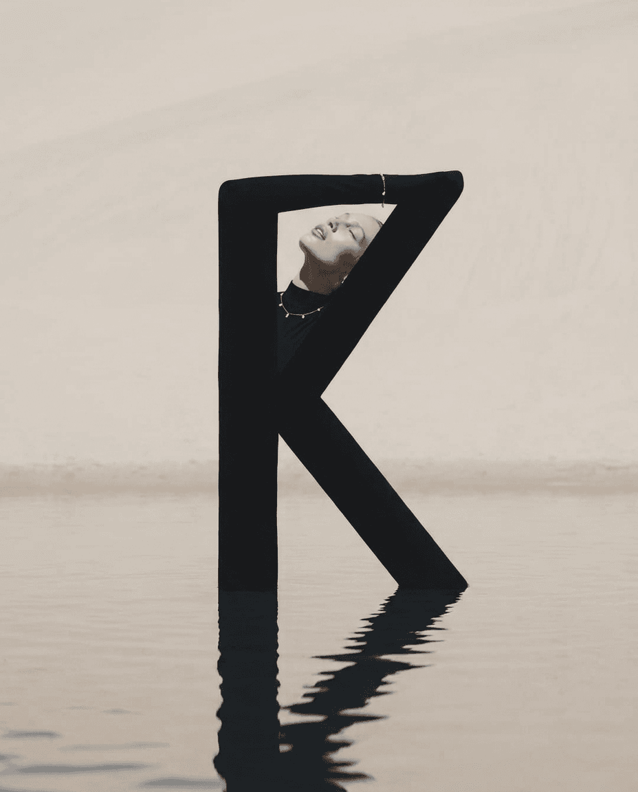 Model posed inside a large black letter K above calm water.