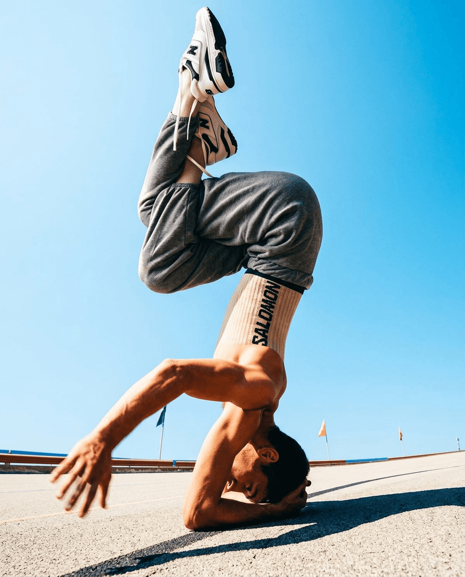 Male dancer in a headstand against a blue sky.