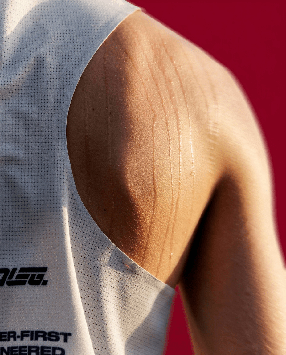 Close-up of an athletic shoulder with sweat droplets on a red background.