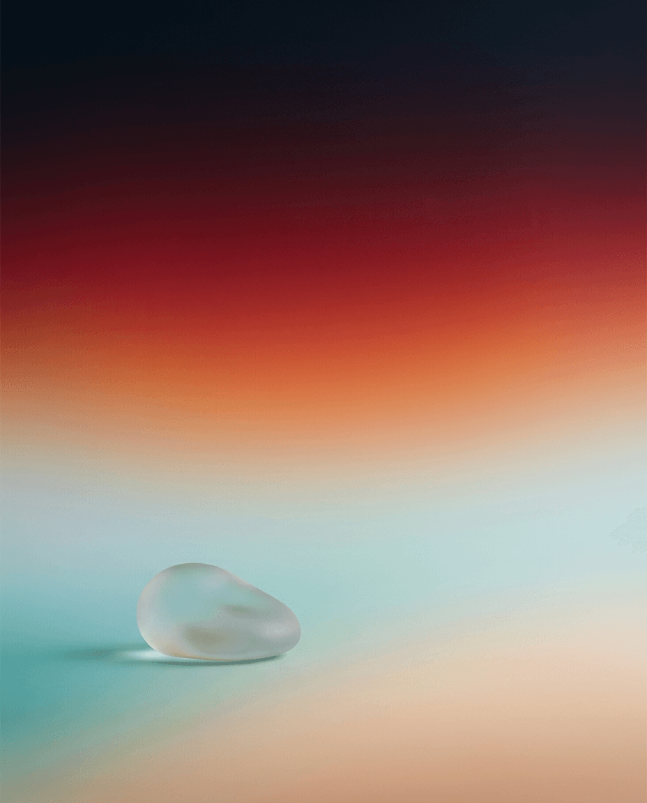 A pebble-shaped glass object on a softly gradient backdrop of oranges and blues.