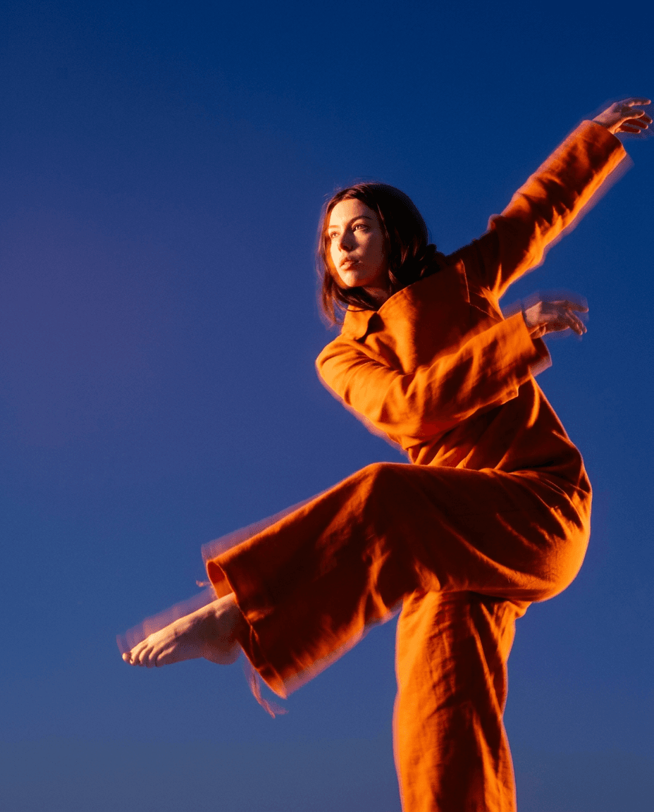 Woman in an orange outfit dancing against a deep blue sky.