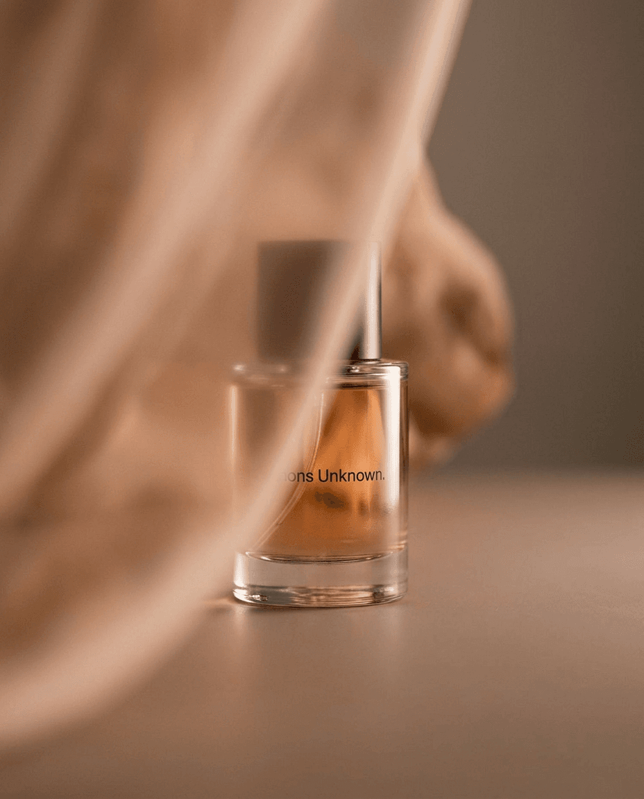 Perfume bottle partially obscured by a sheer curtain in warm tones.