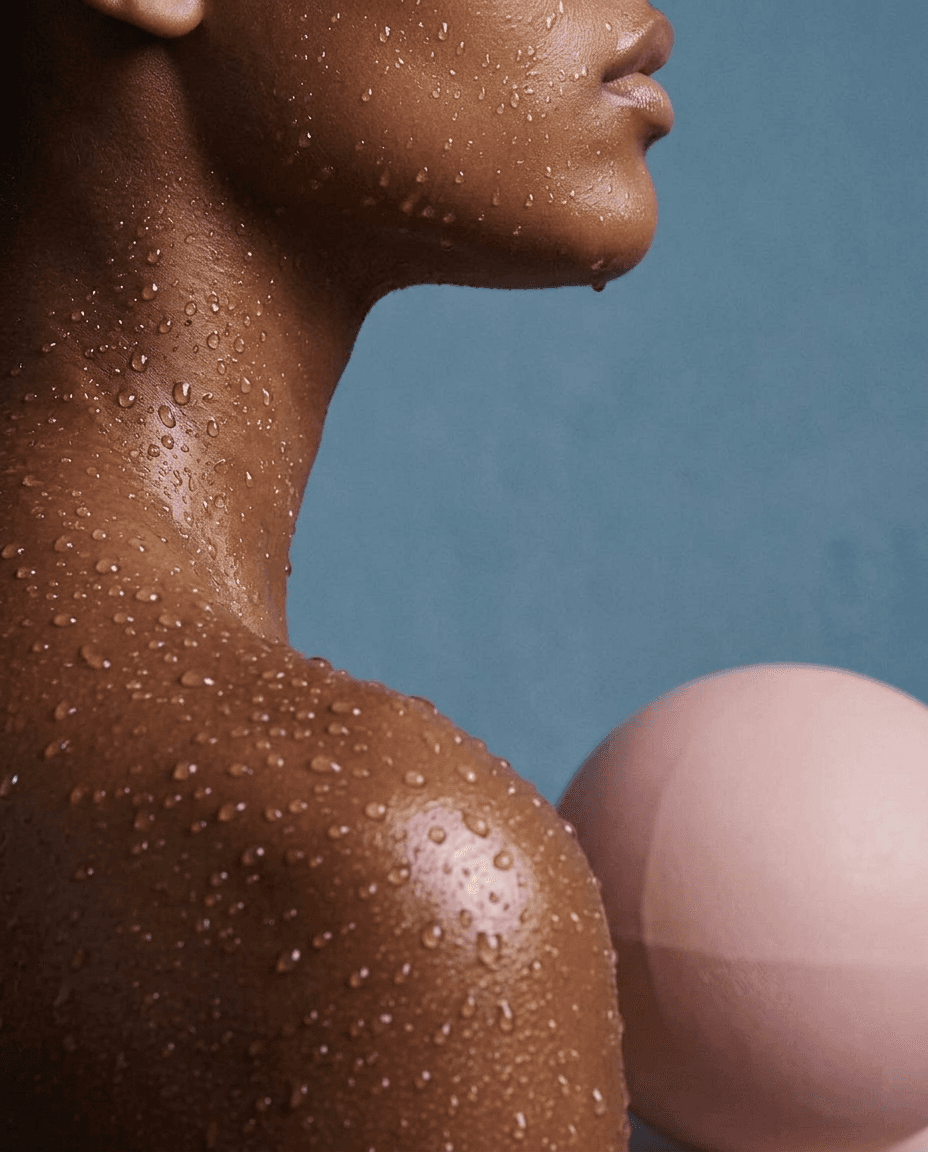 Close-up of glistening skin tone on a blue background with a pink sphere.