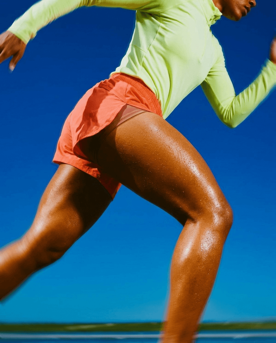 Runner in neon green and coral outfit mid-stride against a blue sky.
