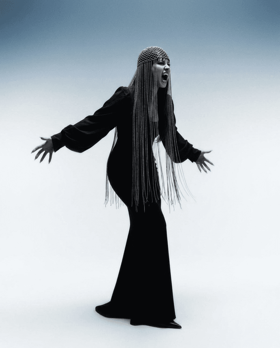Portrait of a figure in a black gown with outstretched arms and a fierce expression.