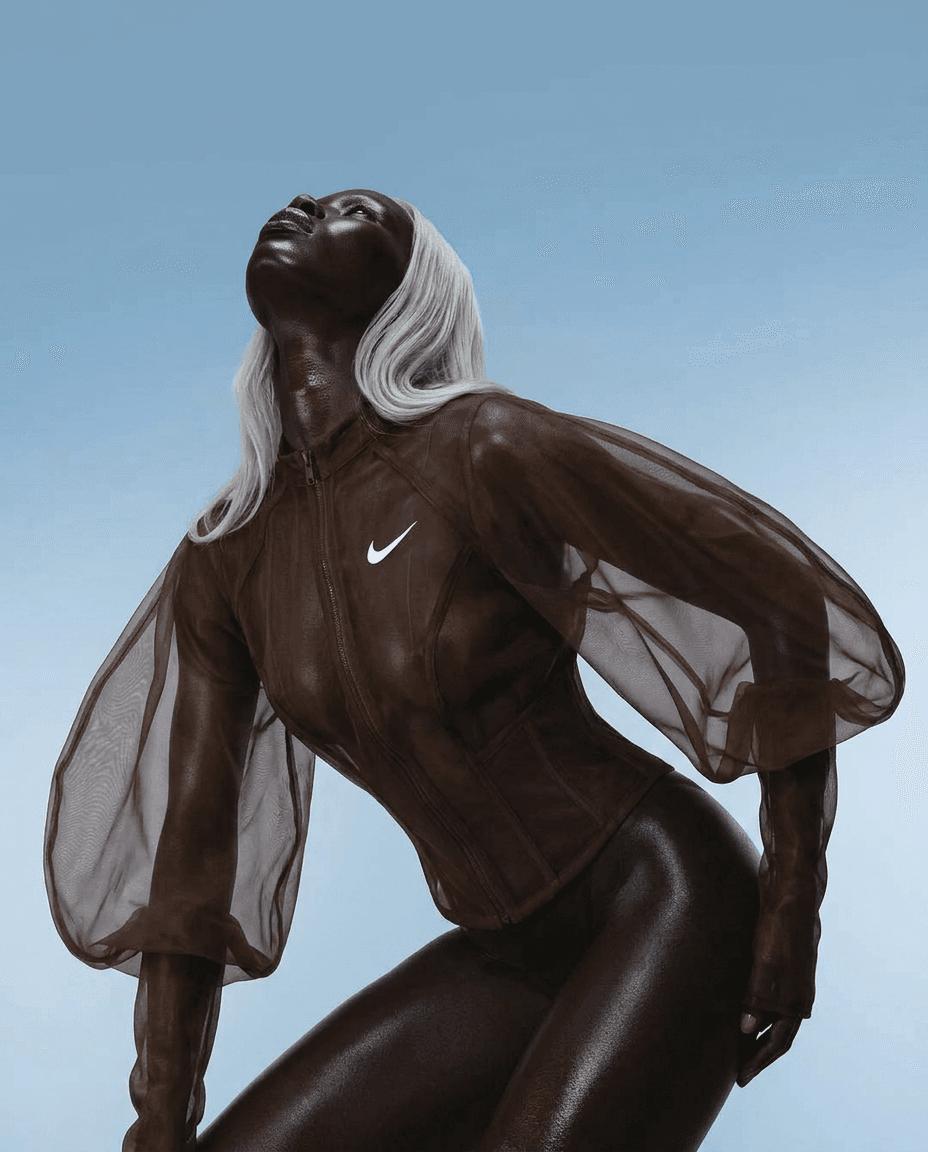 Model with deep brown skin in a sheer chocolate Nike jacket on a blue background.