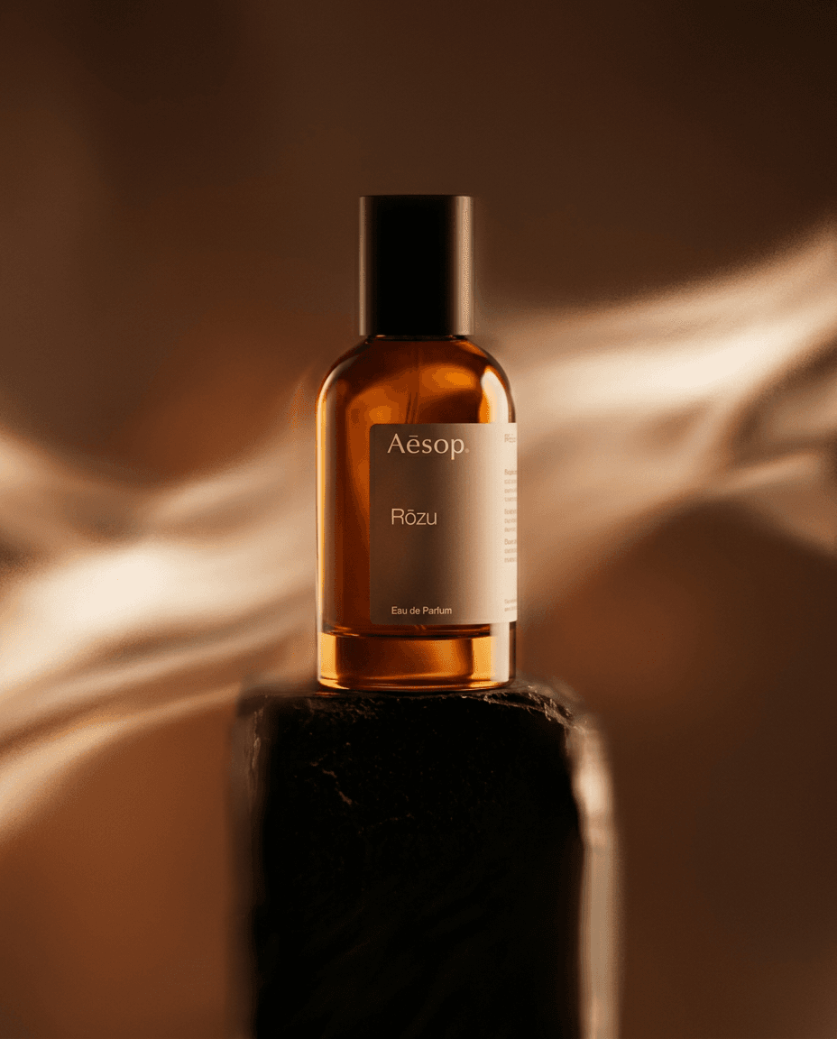Aesop's Rōzu perfume bottle on a dark pedestal with a blurred background.