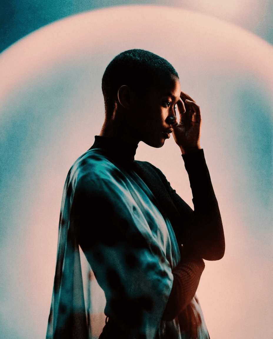 Silhouette of a woman with a shaved head in translucent fabric, surrounded by soft pastel colours.